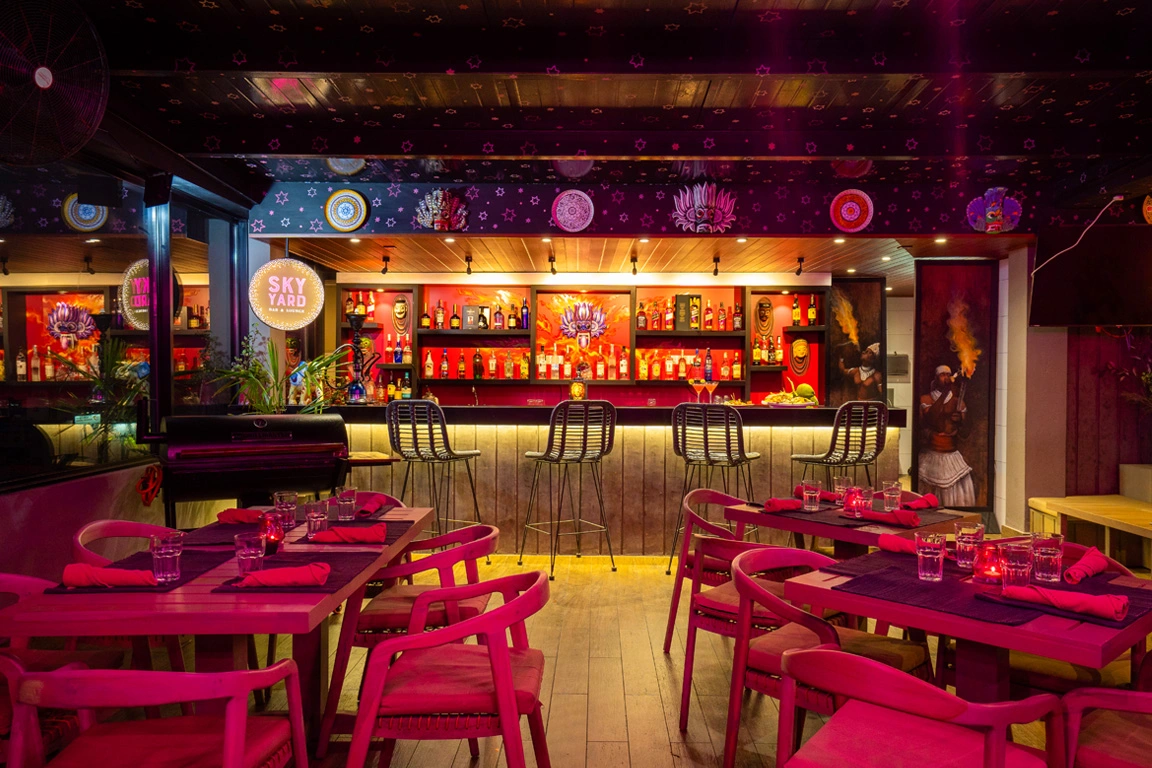 The vibrant interior of the Sky Yard Bar & Lounge, adorned with eclectic artwork and a lively color scheme, offering a cozy and inviting ambiance for social gatherings.