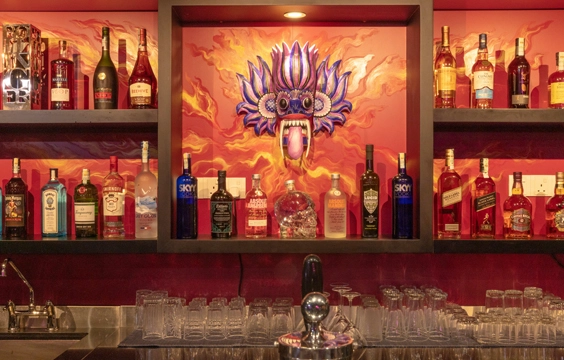 The vibrant Sky Yard Bar & Lounge, with its shelves lined with a variety of liquor bottles, under a striking mural of a mythological creature, and an array of clean glasses ready for patrons.